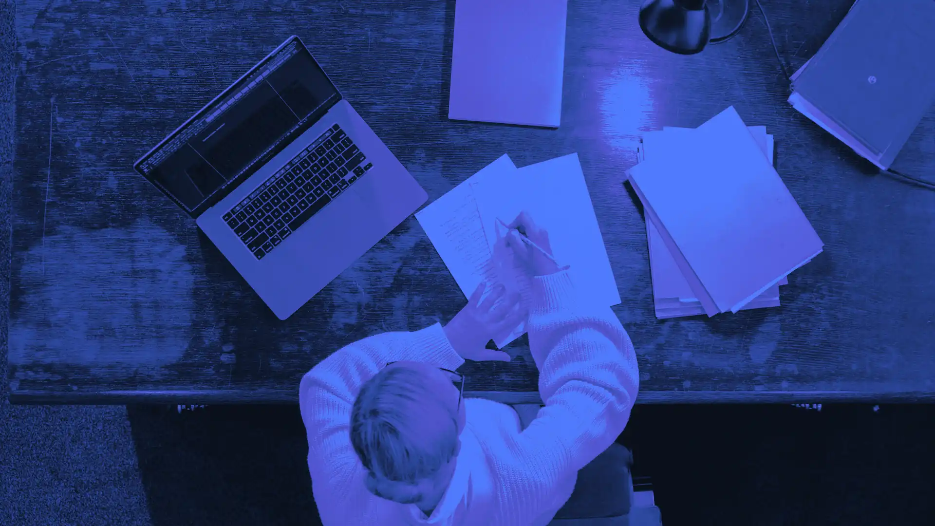 Vue du dessus d’une personne rédigeant des notes à son bureau près d’un ordinateur, pour le blog prospection commerciale