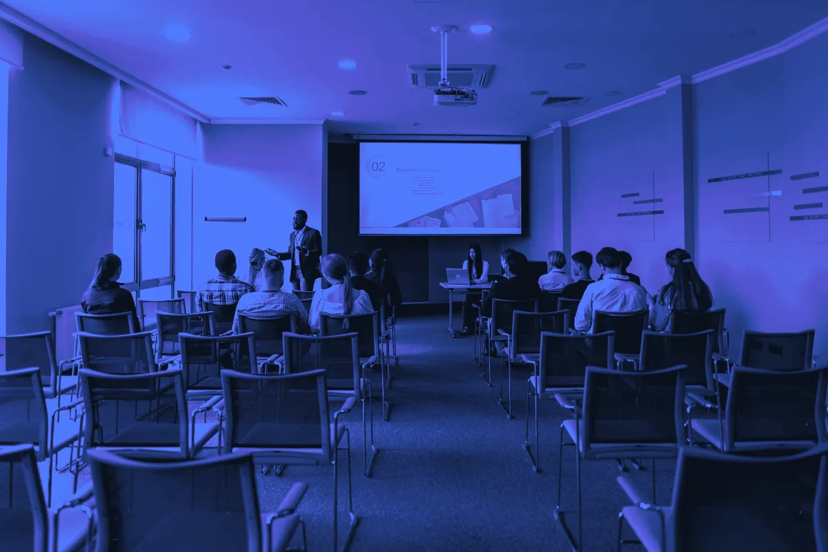 Salle de séminaire avec un formateur devant l’écran de projection et des stagiaires assis : leads formation professionnelle