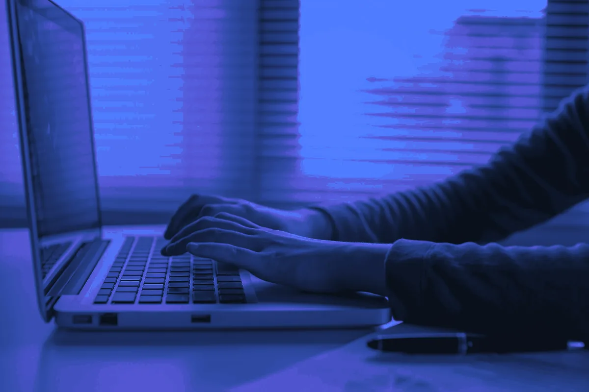 Mains tapant sur le clavier d’un ordinateur portable près d’une fenêtre, en train d’écrire un mail de prospection