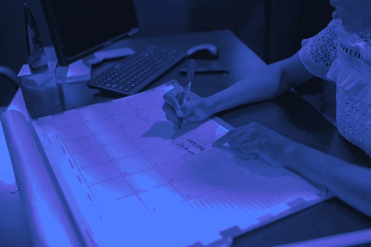 Main notant un créneau dans un grand agenda papier posé sur un bureau, pour la prise de rendez-vous B2B