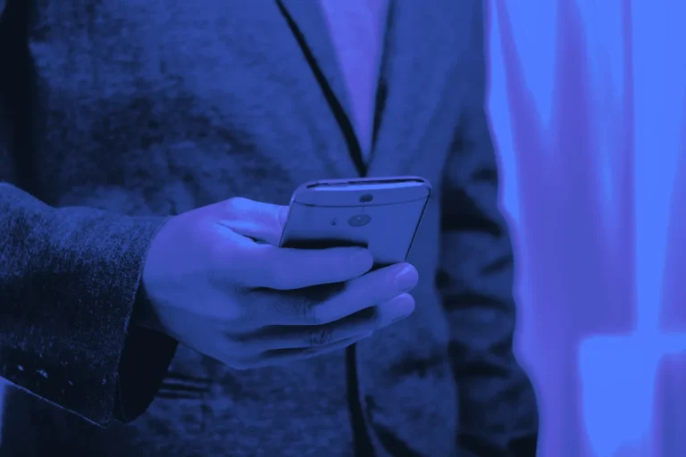 Professionnel en veste consultant son smartphone, le geste quotidien de celui qui veut prospecter sur LinkedIn