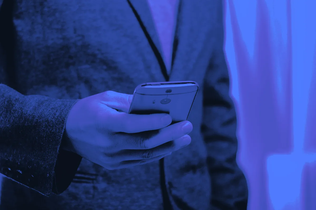 Professionnel en veste consultant son smartphone, le geste quotidien de celui qui veut prospecter sur LinkedIn