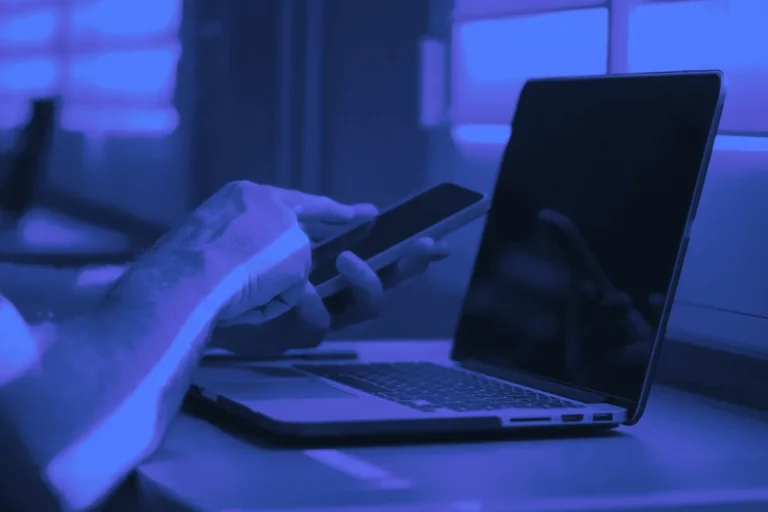 Main tenant un smartphone devant un ordinateur portable ouvert, le poste de travail typique du social selling B2B