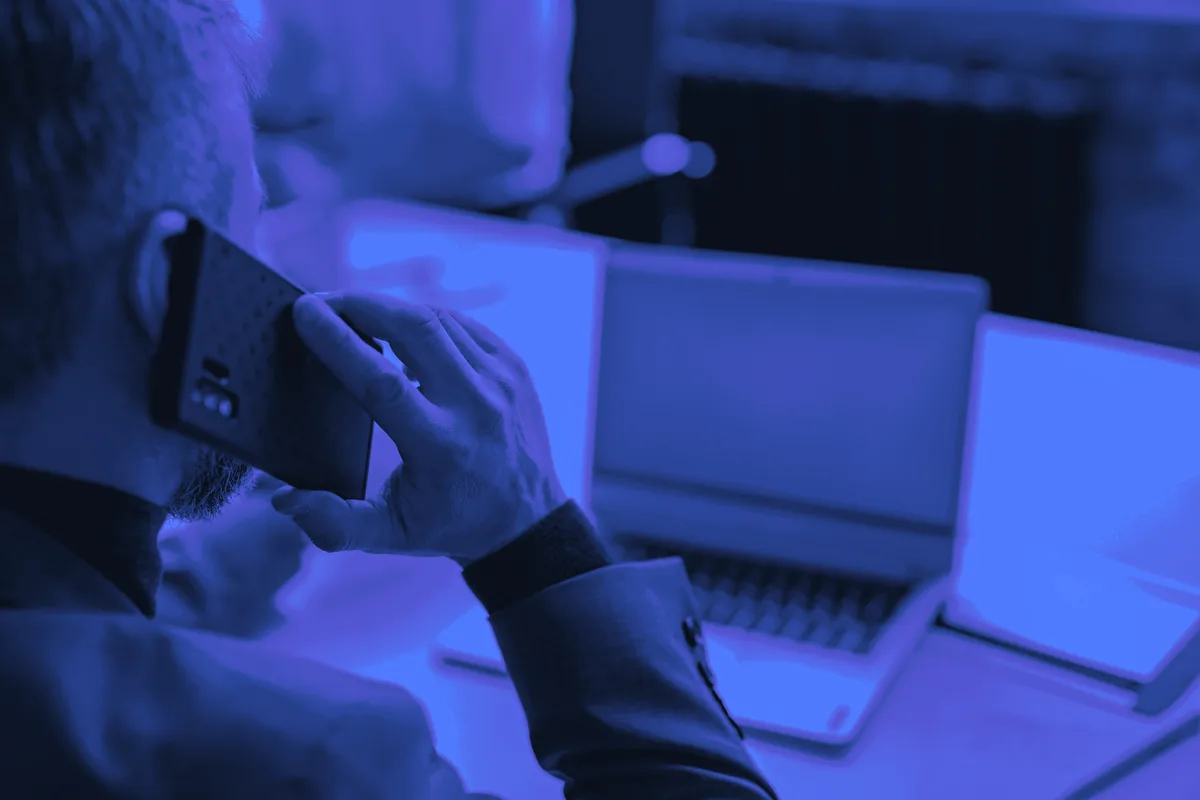 Commercial en téléprospection B2B, téléphone à l’oreille, face à son ordinateur portable pendant un appel